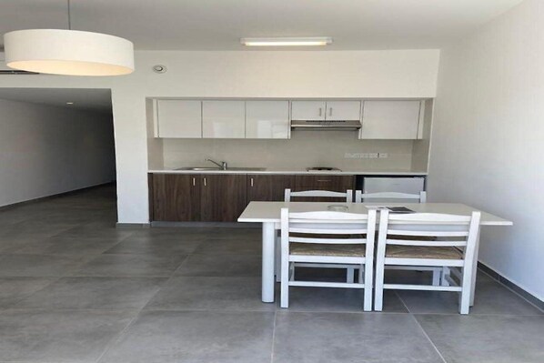 A modern kitchen with white cabinets, a stainless steel sink, and a dining area with a white table and chairs. - Sweet Memories Hotel Apartments (Paralimni)