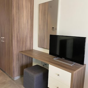 Moderni huone, jossa on televisio puisen jalustan päällä, harmaa rahi ja pystysuorilla raidoilla koristeltu vaatekaappi.
