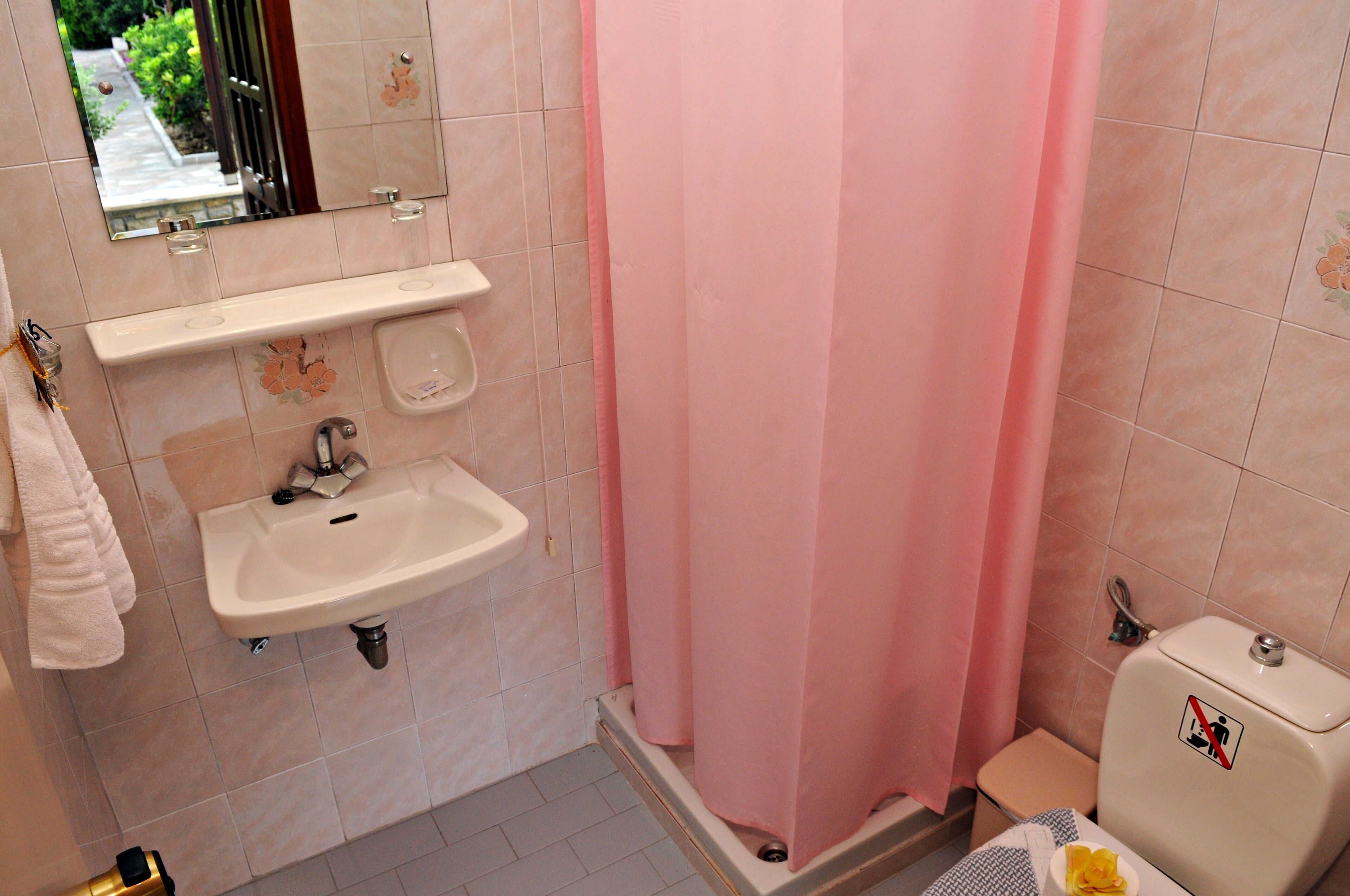 Une salle de bain équipée d’un lavabo, d’un miroir, de toilettes et d’un rideau de douche rose.