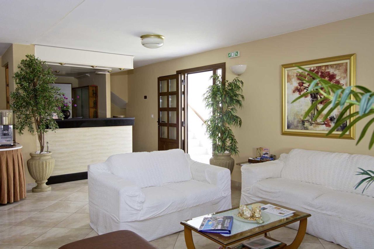 A hotel lobby with two white sofas, a coffee table, potted plants, a reception desk, and a painting on the wall.