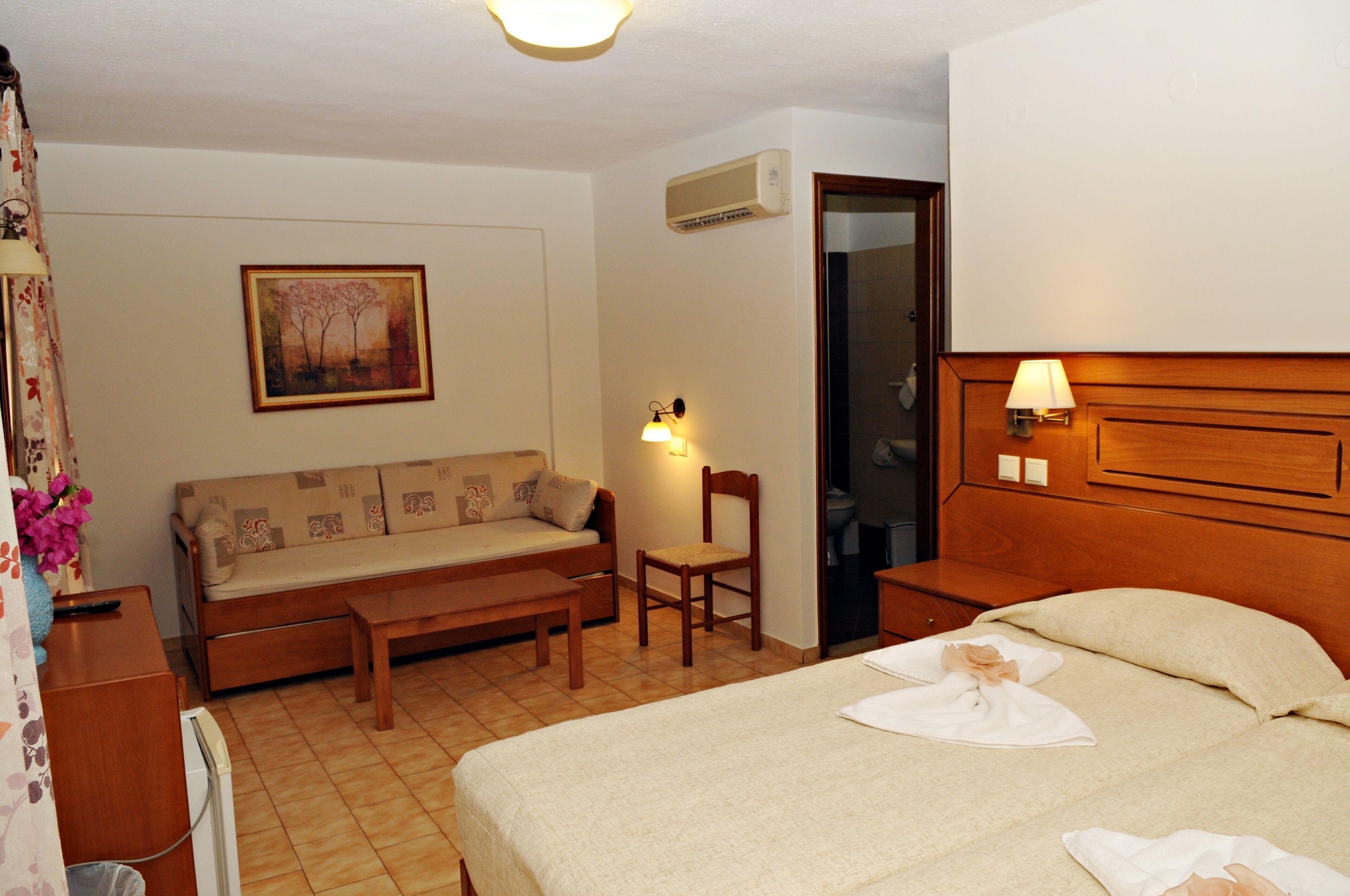 Een hotelkamer met een bed, een bank, een stoel, een klein tafeltje, een lamp en een schilderij aan de muur.