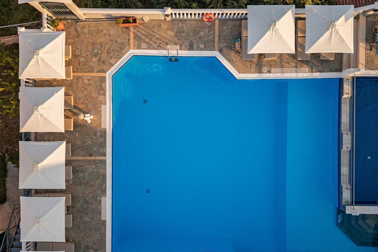 A rooftop swimming pool with a stone deck and white umbrellas.