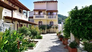 A narrow street with buildings on either side, featuring balconies with railings and potted plants. - Athena Beach (Samos)