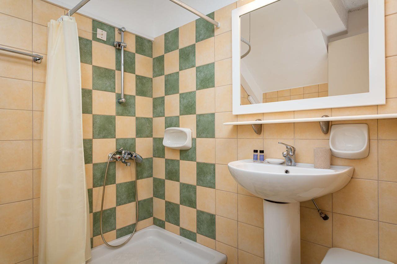 Un bagno con parete rivestita di piastrelle a scacchi, una doccia, un lavandino e uno specchio.