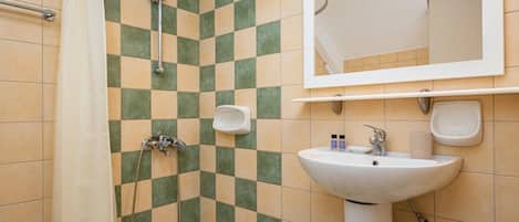 Un bagno con parete rivestita di piastrelle a scacchi, una doccia, un lavandino e uno specchio.