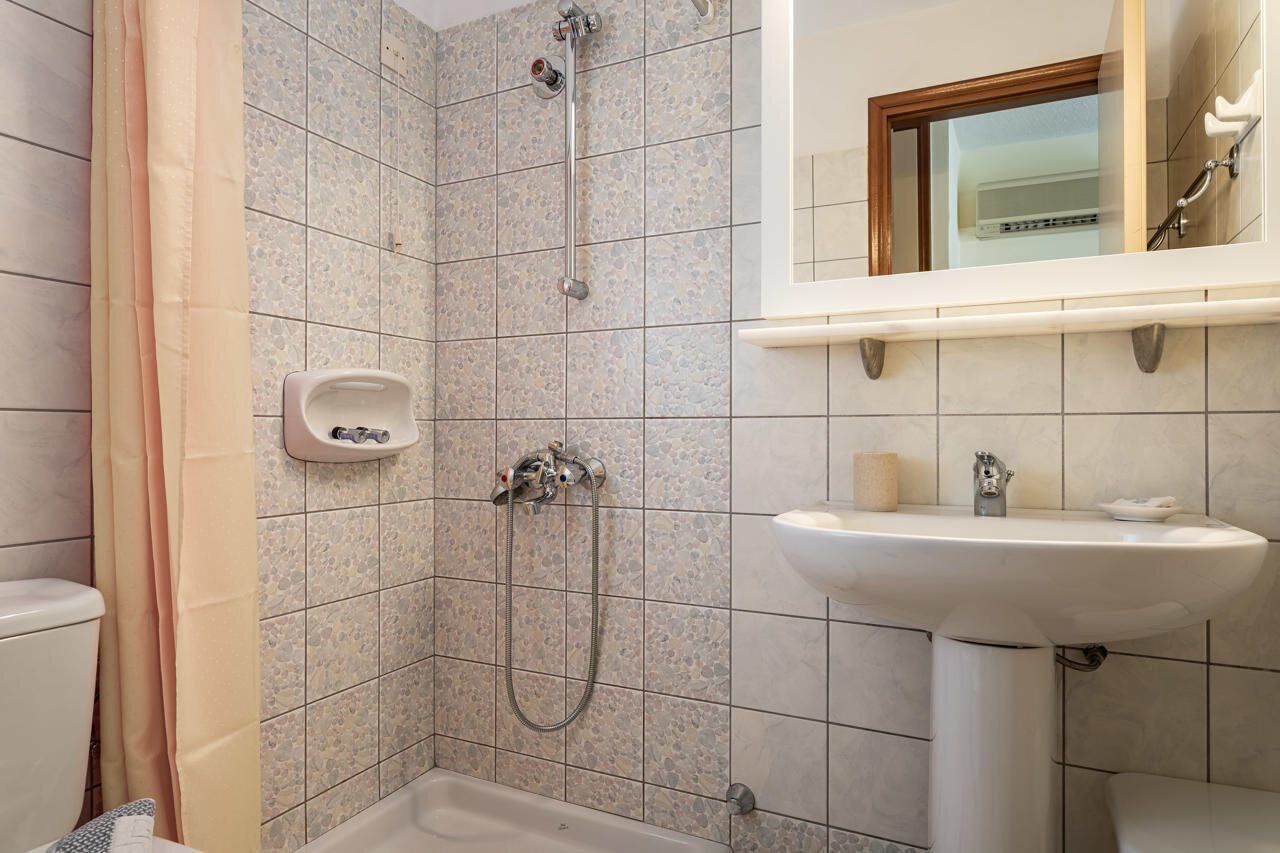 A bathroom with a shower, toilet, sink, and a mirror.