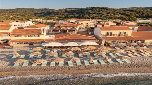 A coastal town with beachside buildings, rows of beach umbrellas, and a clear view of the sea. - Athena Beach (Samos)