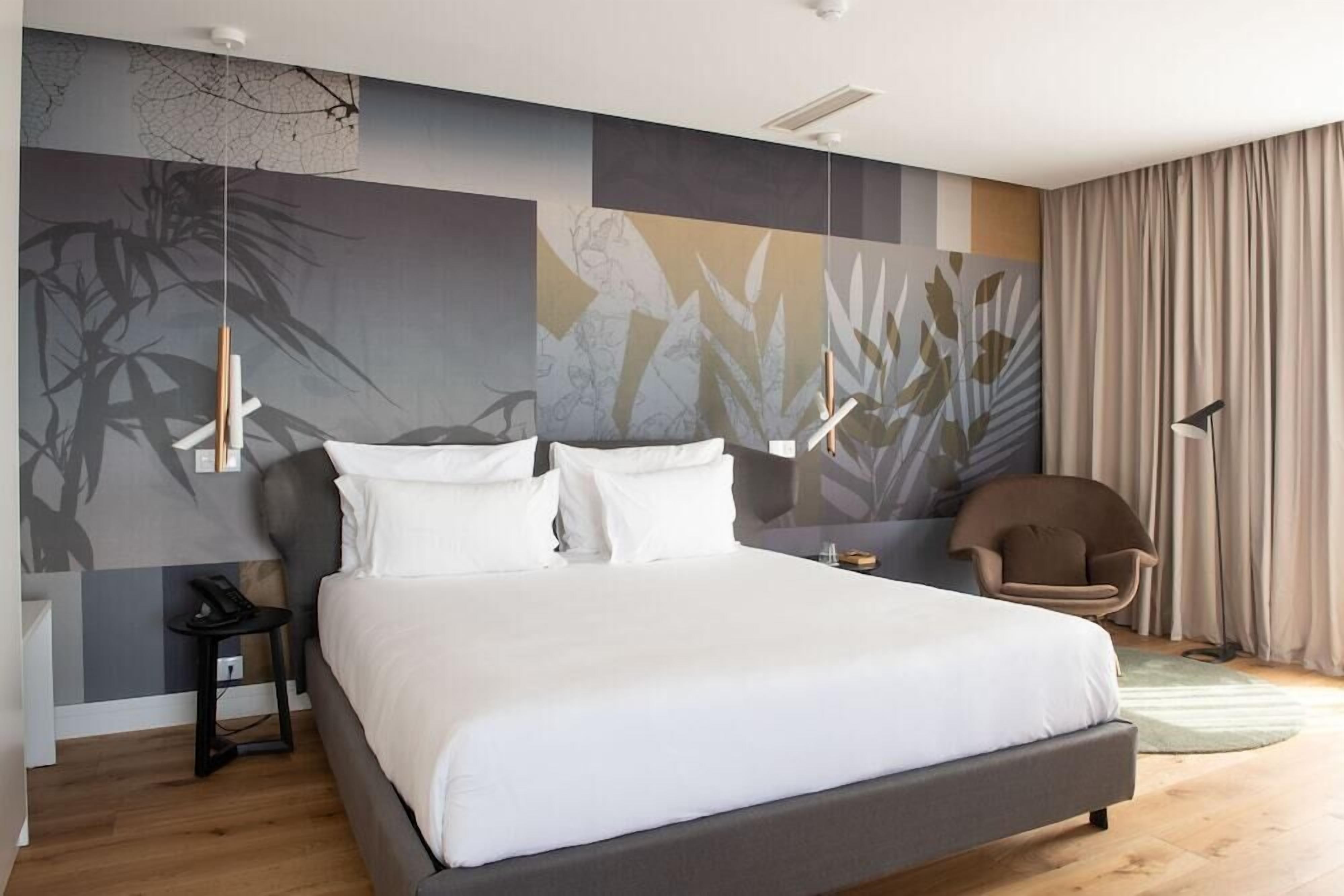 Um quarto moderno com uma cama grande, uma mesinha de cabeceira, uma cadeira e arte abstrata na parede.