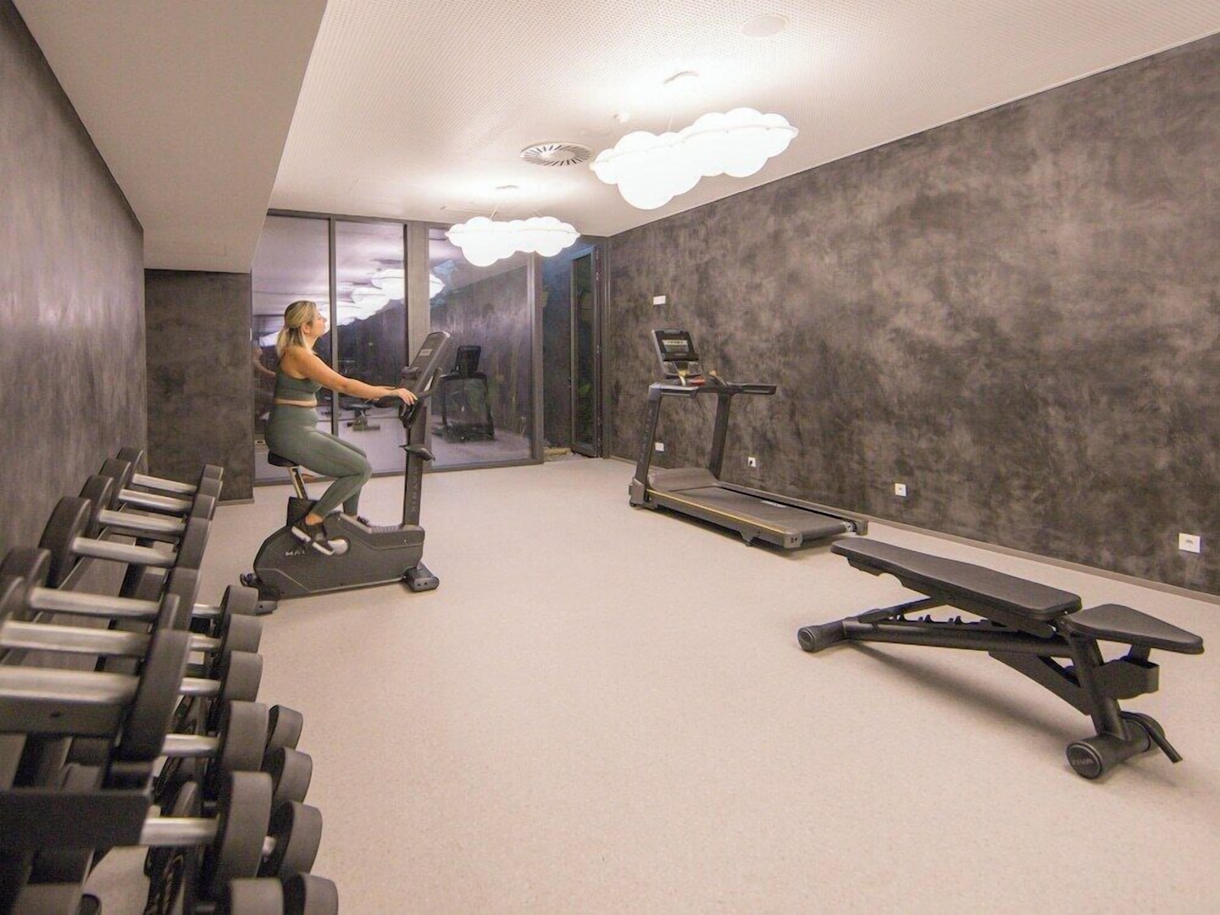 A modern gym with cardio equipment, weight machines, and a bench.