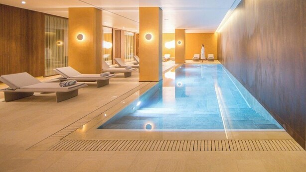 Ein moderner, überdachter Pool mit Liegestühlen und einer Person, die gerade vorbeigeht.