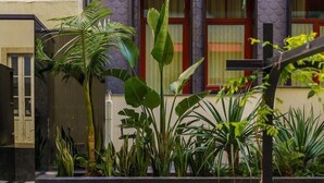Un patio con fuente, plantas en macetas y un edificio con toldos rojos.