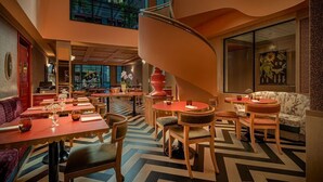 Un restaurante moderno con una escalera espiral central, varias mesas de comedor y un suelo con estampado.