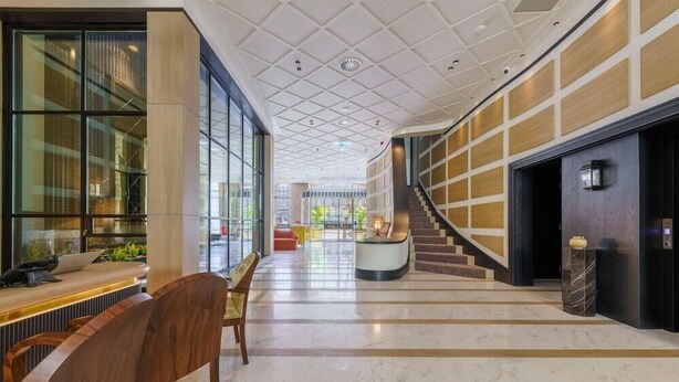 Un vestíbulo amplio con suelo de mármol, mostrador de recepción, una escalera y ventanas grandes.