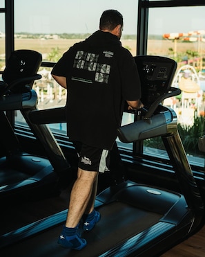 Un homme court sur un tapis de course dans une salle de sport dotée de grandes fenêtres.
