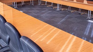 Una sala conferenze con un lungo tavolo, sedie nere e pavimento rivestito di moquette.