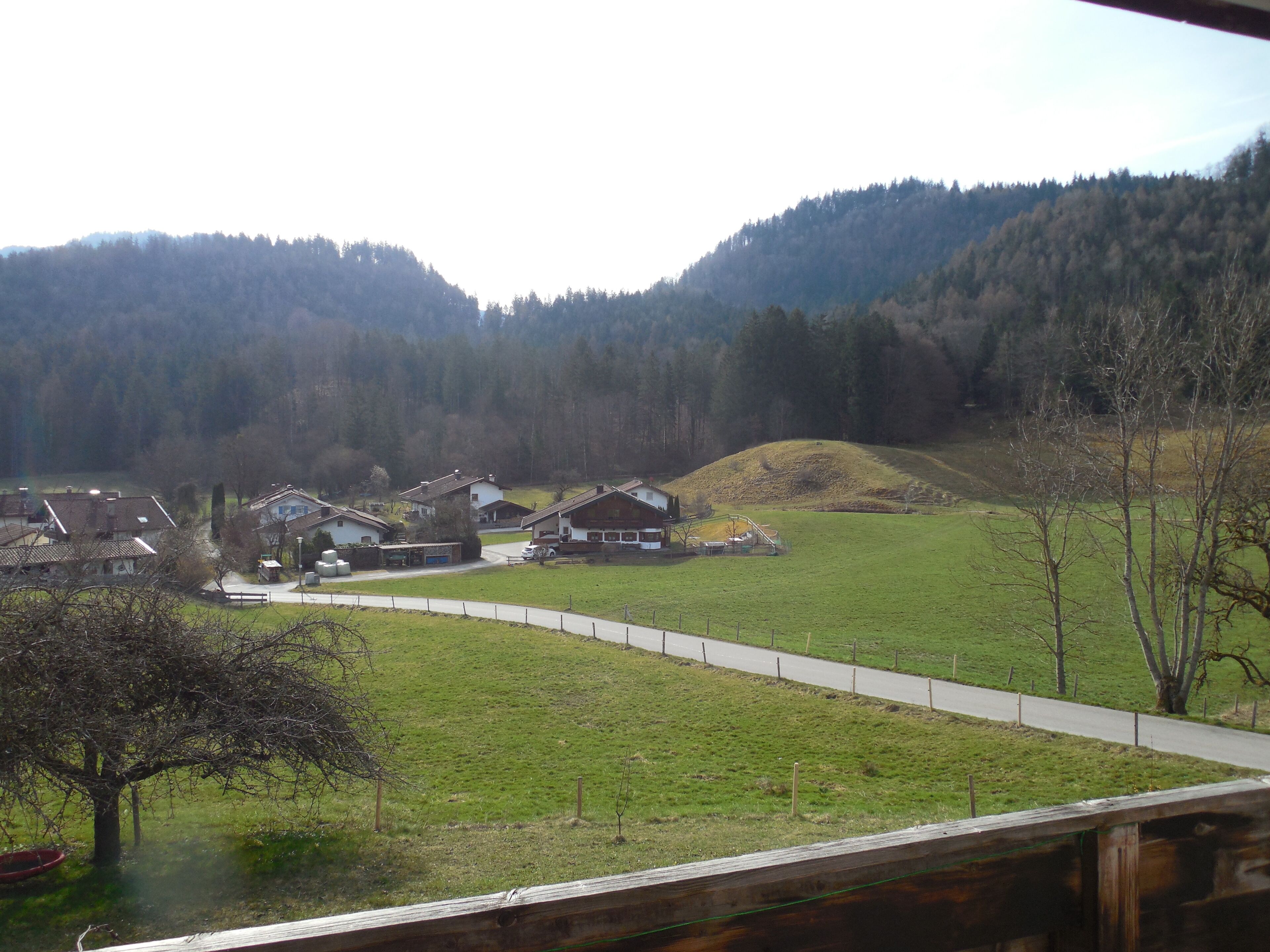 A rural landscape with houses, a winding road, and a forested hill in the background.