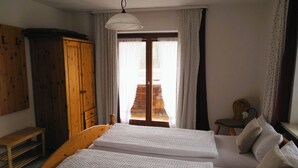 A bedroom with a wooden bed, a wooden wardrobe, a bench, and a window with curtains. - Vacation apartment 60 sqm, 2-4 persons, 2 bedrooms, eat-in kitchen, 2 bathrooms (Unterwössen)