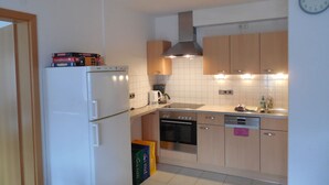 A kitchen with a refrigerator, oven, stove, and a clock on the wall. - Vacation apartment 60 sqm, 2-4 persons, 2 bedrooms, eat-in kitchen, 2 bathrooms (Unterwössen)