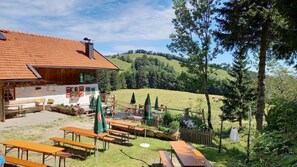 A rustic building with outdoor seating and a view of a green hillside. - Vacation apartment 60 sqm, 2-4 persons, 2 bedrooms, eat-in kitchen, 2 bathrooms (Unterwössen)