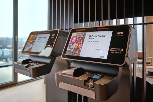 Two self-service kiosks in a hotel lobby with screens displaying welcome messages and options for guests. - Zleep Hotel Vejle (Vejle)