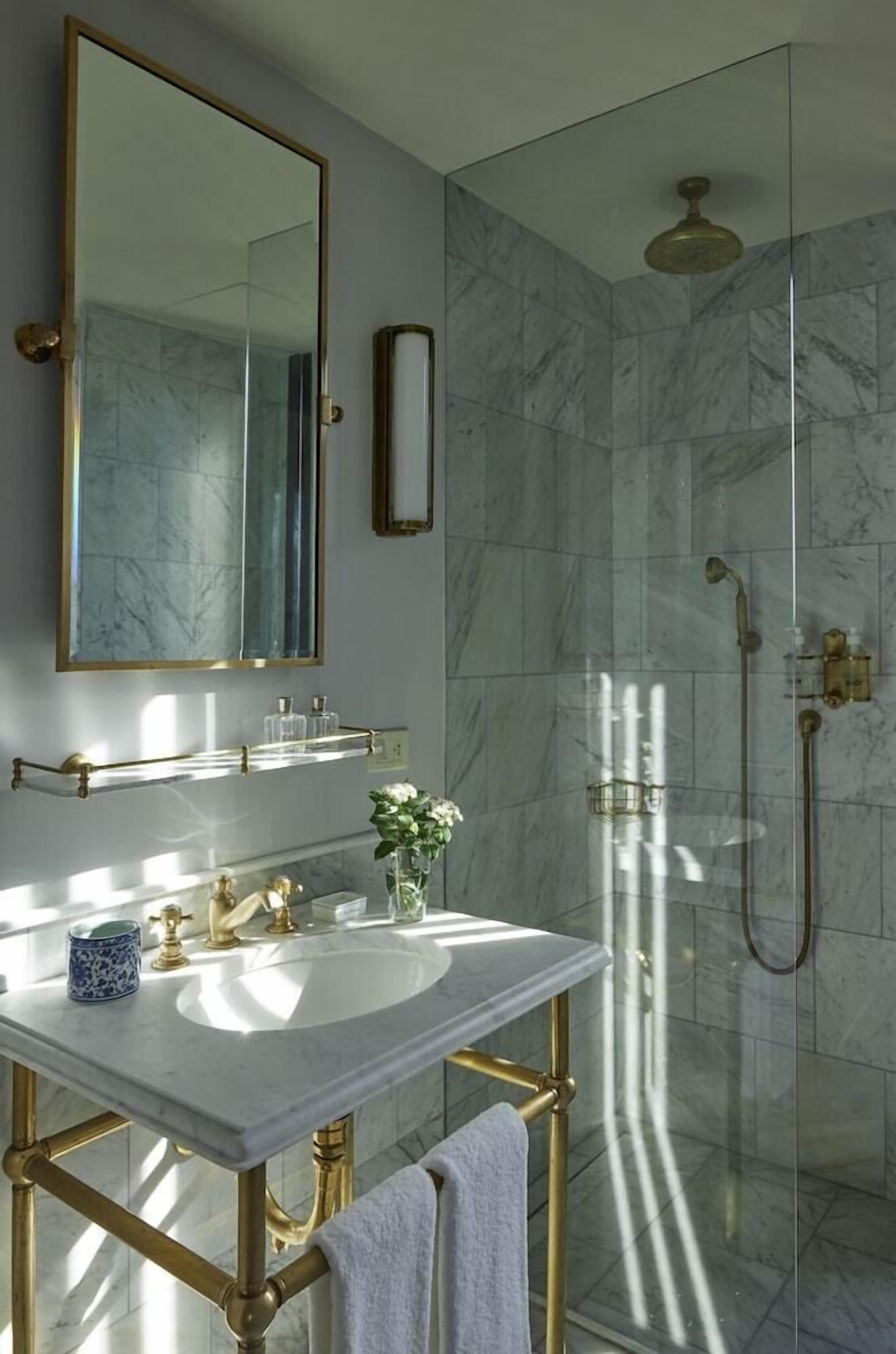 Un baño con lavamanos de mármol, detalles dorados, un espejo grande y una cabina de ducha de vidrio.