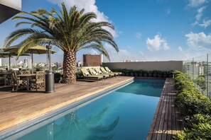 Piscina en la azotea con sillas de descanso, una palmera y vistas a la ciudad.