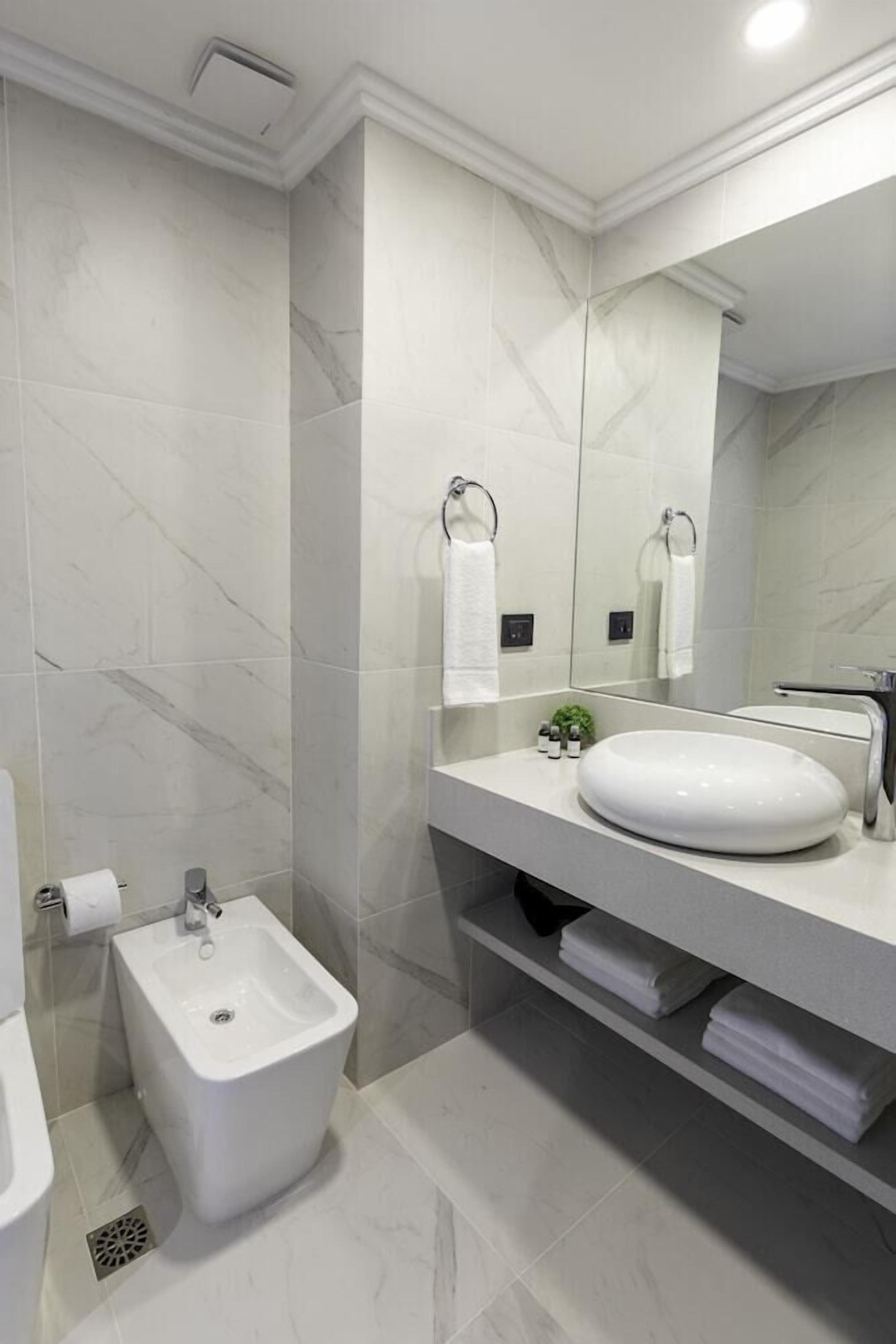 Un baño moderno con bidé, un espejo grande y un lavabo blanco.