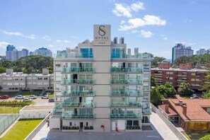 Un hotel moderno con fachada de vidrio, varios balcones y un llamativo logotipo 'S' en la parte superior.
