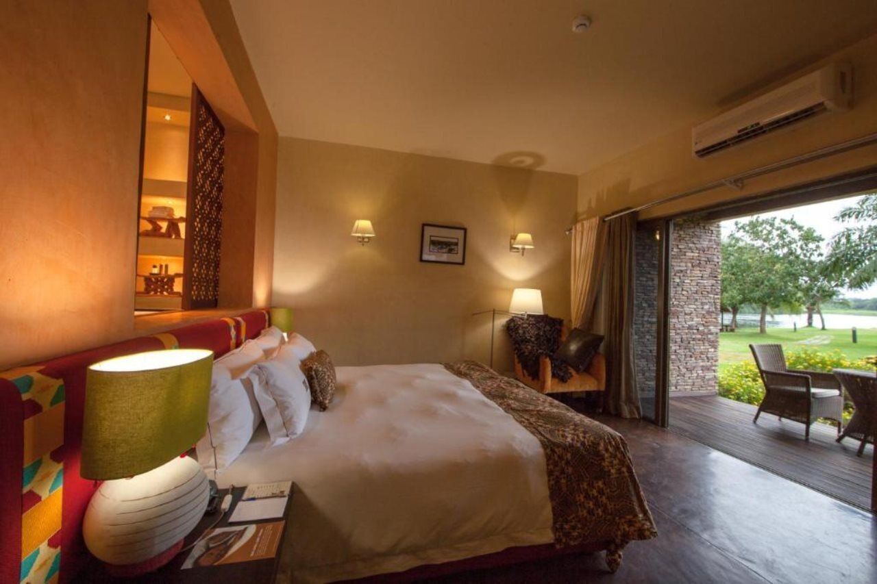 Habitación de hotel con una cama grande, zona de estar con vistas y balcón con mobiliario exterior.
