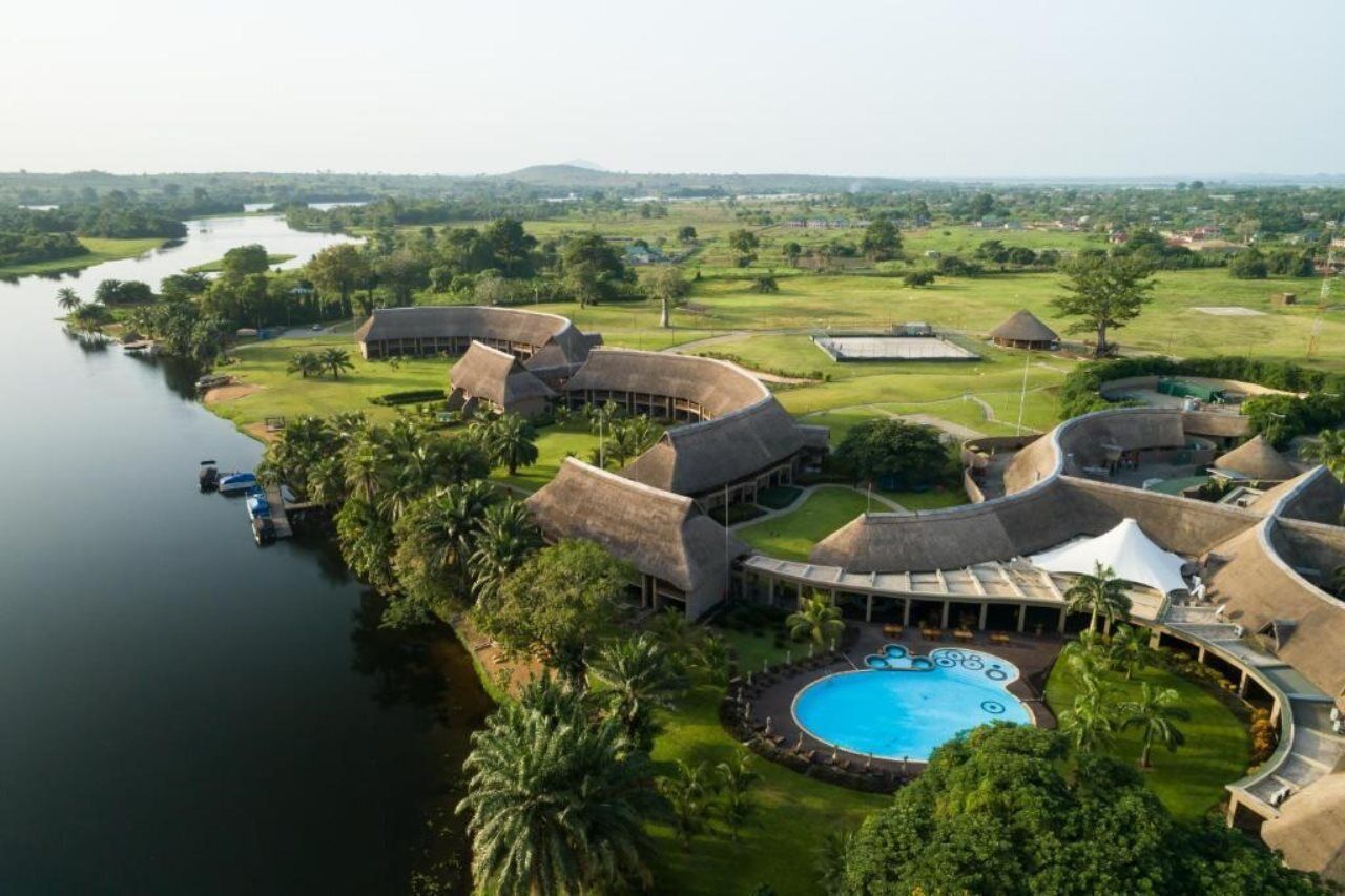 Un resort con edificios de techo de paja, una piscina y vista al río.