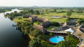 Un resort con edificios de techo de paja, una piscina y vista al río.