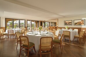 A spacious dining area with round tables, wicker chairs, and large windows offering a view of the surrounding landscape. - Moire Hoi An, Vignette Collection (Hoi An)