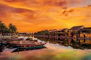Un río tranquilo con barcas tradicionales amarradas, reflejando los edificios y las palmeras circundantes.