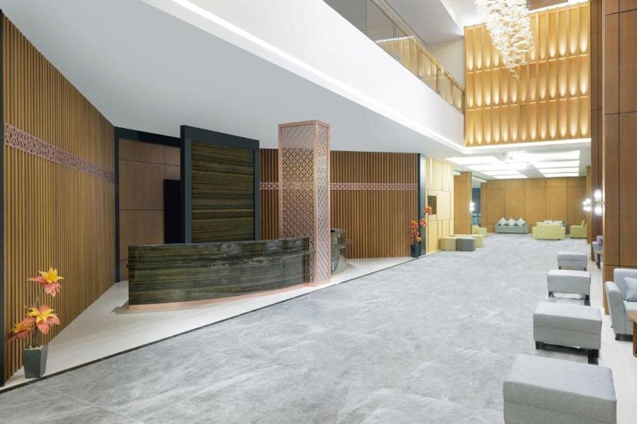 A spacious lobby with a reception desk, seating area, and a high ceiling with a modern chandelier.