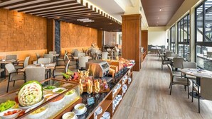 A buffet area with a variety of food items, a seating area with tables and chairs, and a view of the outside through large windows. - FOX Harris Hotel and Convention Banjarnegara (Banjarnegara)