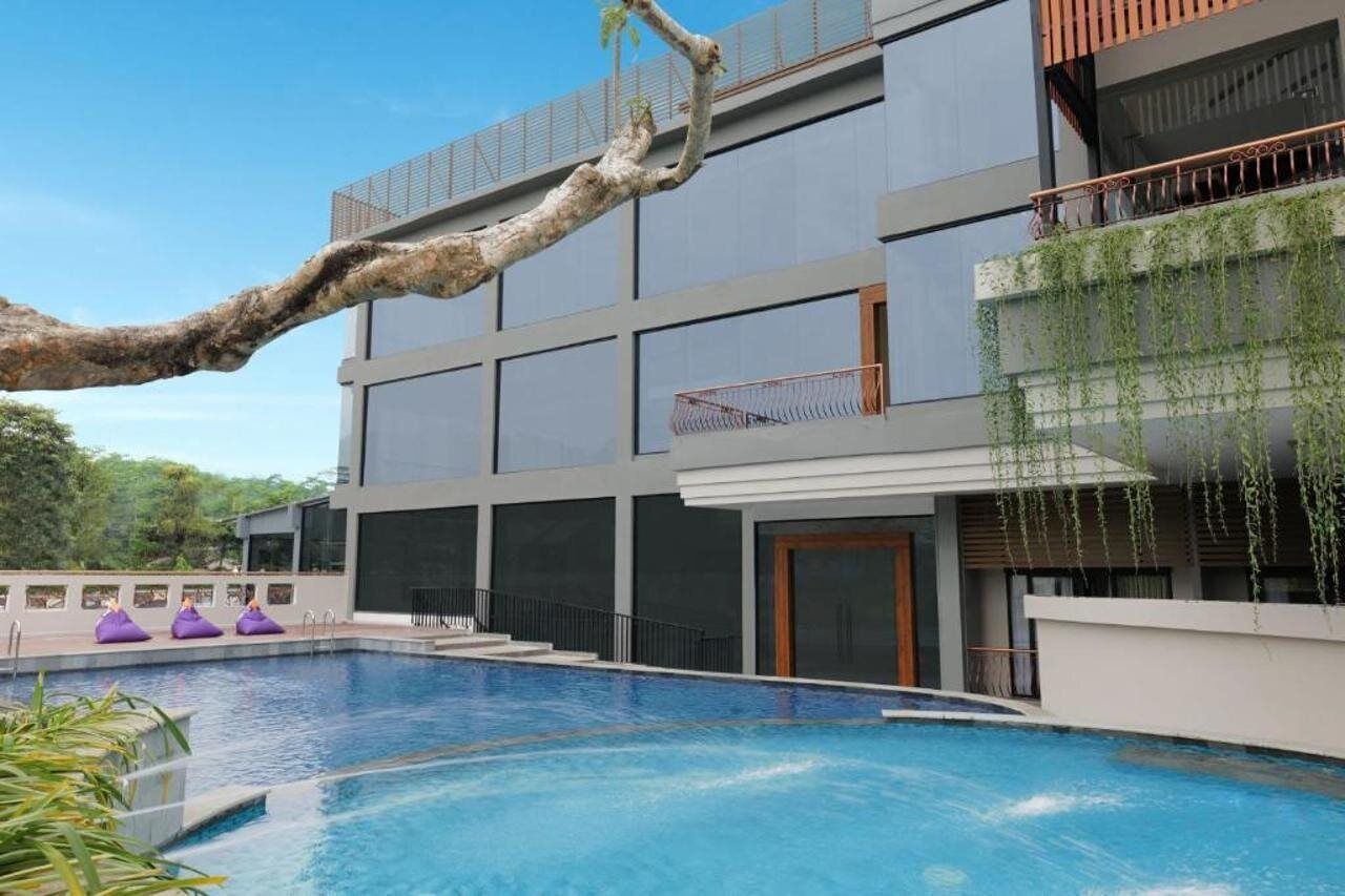 A modern building with a swimming pool, large windows, and a balcony with hanging plants.