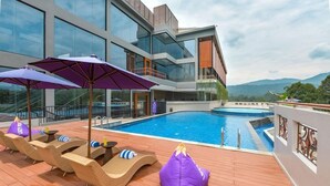 A rooftop pool area with lounge chairs and umbrellas, a swimming pool, and a view of mountains. - FOX Harris Hotel and Convention Banjarnegara (Banjarnegara)