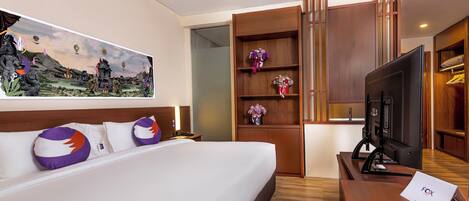 A hotel room with a bed, a TV, a desk, and a painting on the wall.