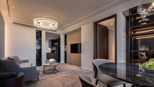 A modern living room with a chandelier, a dining area with a marble table, and a kitchen in the background. - Crowne Plaza Danang City Centre by IHG (Da Nang)