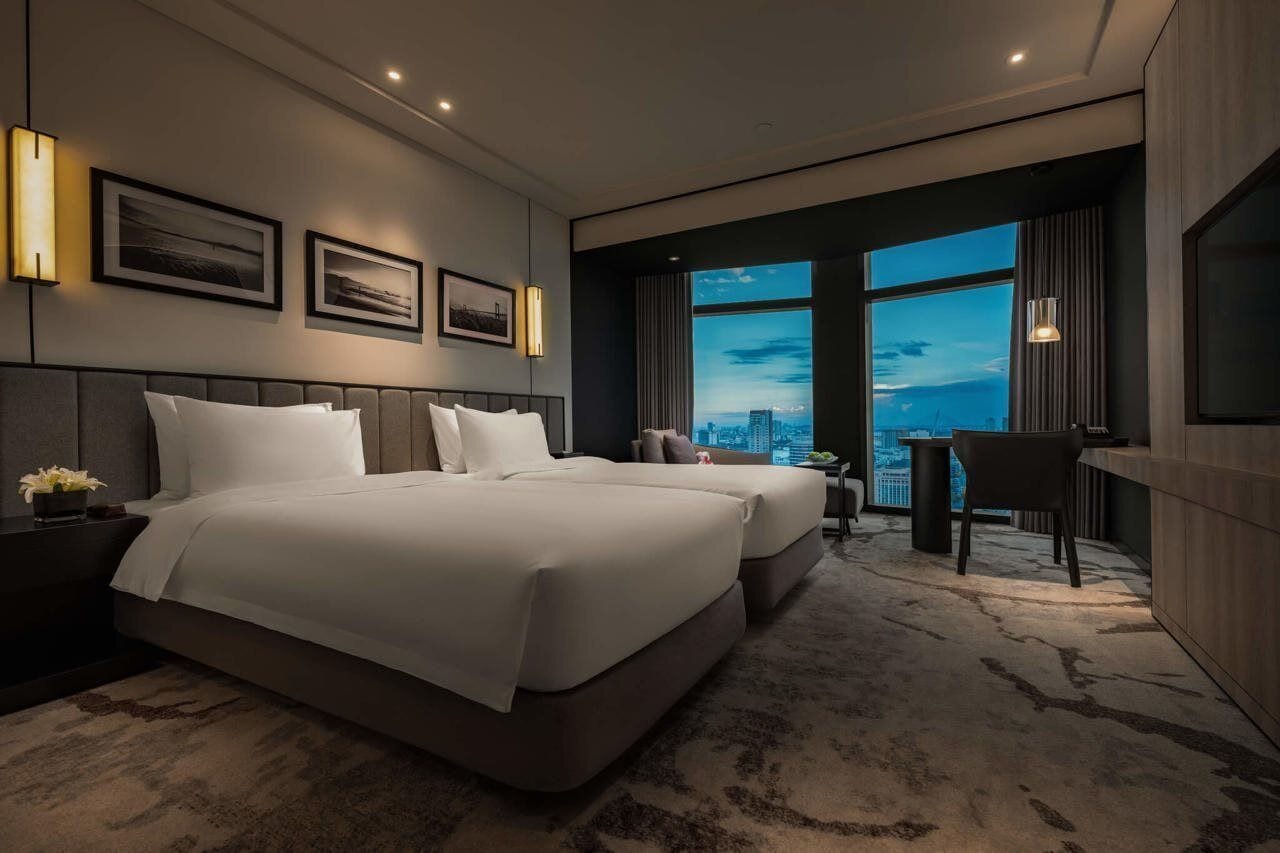 Ein modernes Hotelzimmer mit zwei Betten, einem Schreibtisch und Blick auf die Stadtlandschaft.