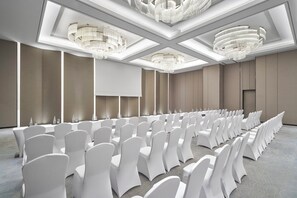 A conference room with rows of white chairs, a large screen, and modern chandeliers. - Crowne Plaza Danang City Centre by IHG (Da Nang)