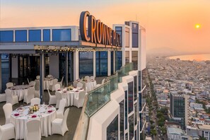 A rooftop restaurant with a view of the city and the ocean at sunset. - Crowne Plaza Danang City Centre by IHG (Da Nang)