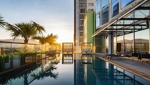 A rooftop infinity pool with lounge chairs, palm trees, and a modern building in the background. - Crowne Plaza Danang City Centre by IHG (Da Nang)