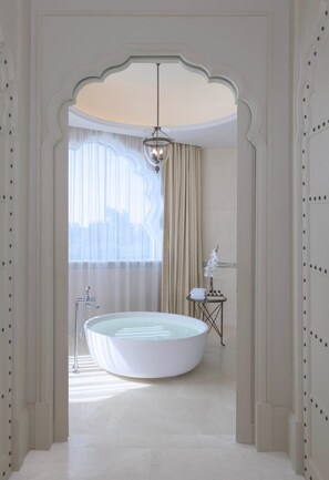 A spacious bathroom with a freestanding bathtub, a vanity with a mirror, and a small table with toiletries. - The Chedi Katara Hotel and Resort - a GHM Hotel (Doha)