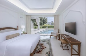 A hotel room with a bed, a desk, a TV, and a view of a pool and garden. - The Chedi Katara Hotel and Resort - a GHM Hotel (Doha)
