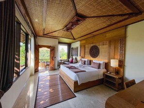 A spacious bedroom with a large bed, a wooden headboard, a bedside table with a lamp, and a view of the outdoors. - Sakti Garden Resort and Spa (Ubud)