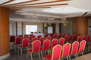 A conference room with rows of red chairs and a white table, wooden paneling, and hanging spherical chandeliers. - Xanadu Makadi Bay (Makadi Bay)