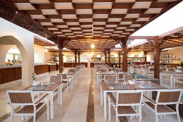 A spacious dining area with multiple tables and chairs, a central bar, and a ceiling with a wooden grid pattern. - Xanadu Makadi Bay (Makadi Bay)