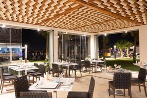 An outdoor dining area with tables and chairs, a wooden ceiling, and large windows. - Xanadu Makadi Bay (Makadi Bay)