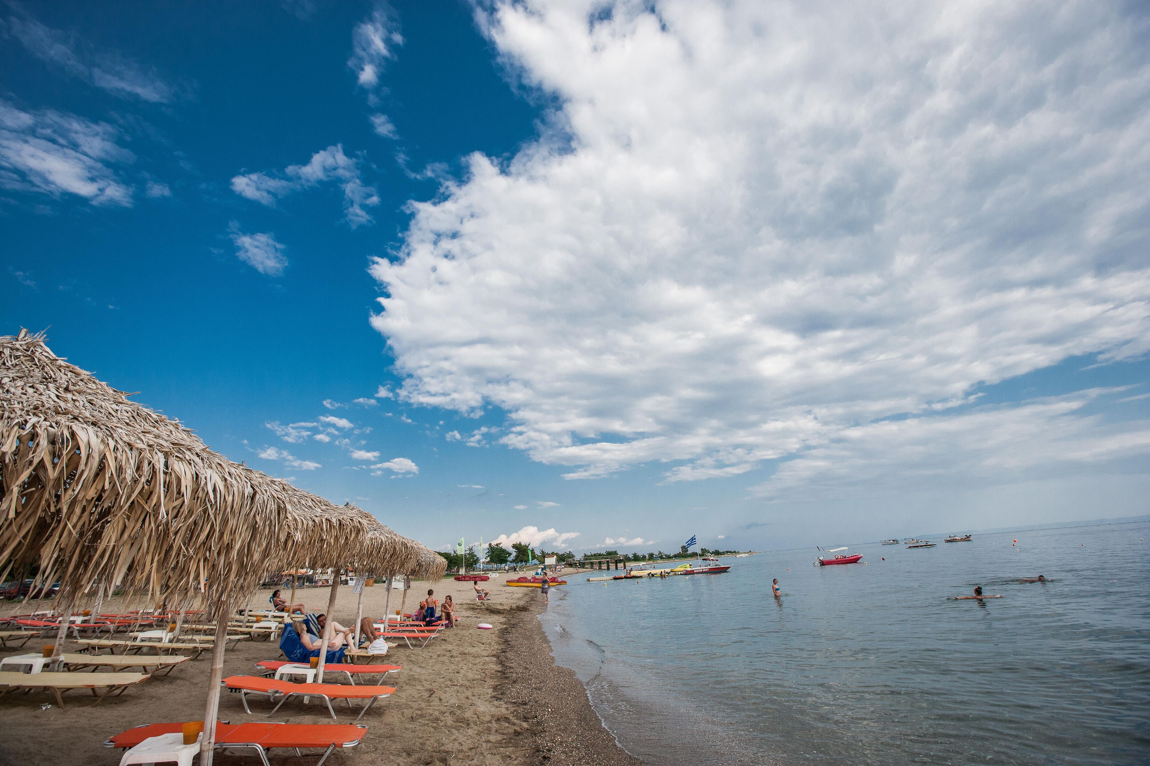 A beach with thatched umbrellas, sun loungers, and calm water.